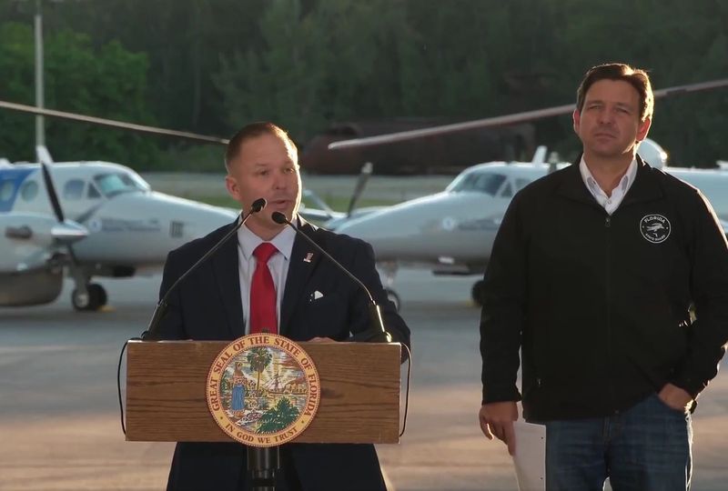 Department of Homeland Security Senior Counselor Keith Pearson (left) speaks Feb. 26, 2025, as Florida Gov. Ron DeSantis (right) watches at Homestead Air Force Base.