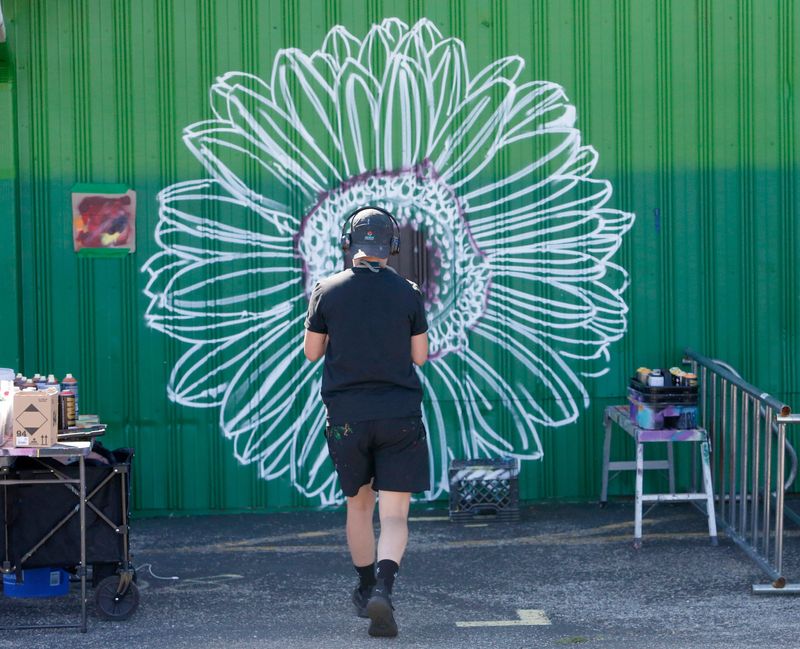 Artist Alex Ann Allen walks toward the sketch of a large flower she is painting Thursday, May 30, 2024, at the South Bend Farmer's Market. A mural is being painted on the northwest wall of the market in celebration of the venue’s 100th anniversary.
