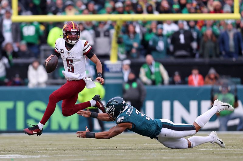 FILE PHOTO: Jan 26, 2025; Philadelphia, PA, USA; Washington Commanders quarterback Jayden Daniels (5) leaps to avoid the tackle of Philadelphia Eagles linebacker Nolan Smith Jr. (3) during the first half of the NFC Championship game at Lincoln Financial Field. Mandatory Credit: Bill Streicher-Imagn Images/File Photo