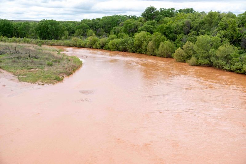 The Canadian River winds through green brush north of Amarillo off U.S. Highway 287 on May 7, swollen and muddy after several days of heavy rain across the Texas Panhandle.
