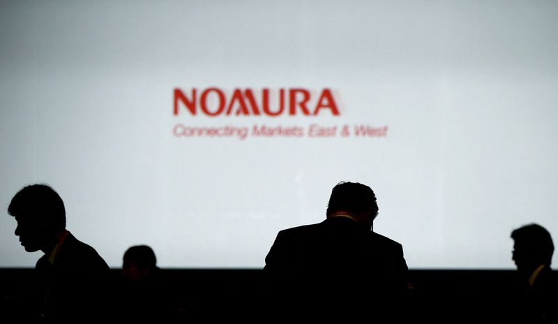 FILE PHOTO: Investors stand in front of a screen showing the logo of Nomura Holdings in Tokyo