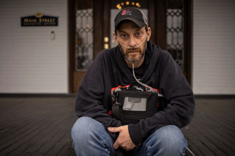 Josh Cochran, 45, an underground coal miner with more than 20 years of experience, holds his portable oxygen concentrator while sitting outside a law office in Oak Hill, West Virginia, U.S., April 10, 2025. REUTERS/Adrees Latif