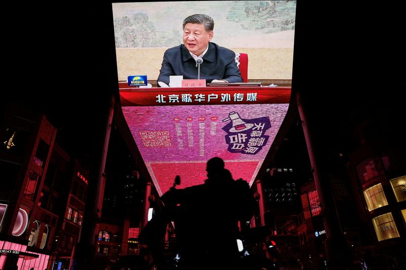 FILE PHOTO: A man rides a scooter past a giant screen showing news footage of Chinese President Xi Jinping attending a Chinese Communist Party politburo meeting, in Beijing, China December 9, 2024. REUTERS/Tingshu Wang/File Photo