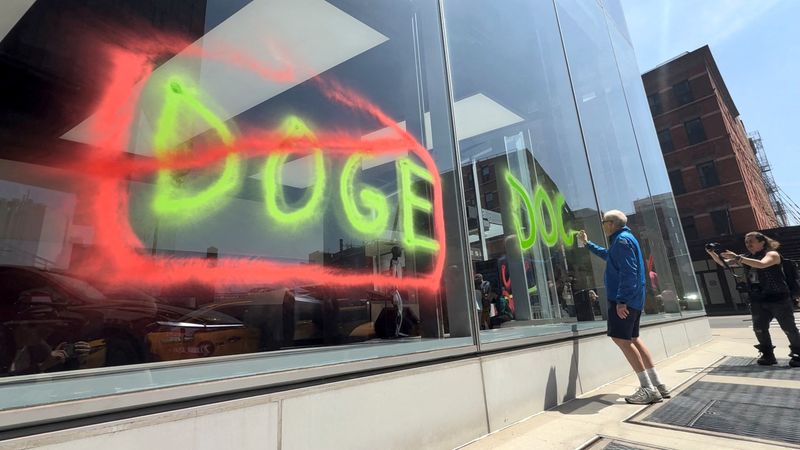 FILE PHOTO: A man sprays paint graffiti against Elon Musk's Department of Government Efficiency (DOGE) on a Tesla showroom in New York, U.S., April 22, 2025, in this still image taken from video.    Extinction Rebellion NYC/Handout via REUTERS    THIS IMAGE HAS BEEN SUPPLIED BY A THIRD PARTY. NO RESALES. NO ARCHIVES. MANDATORY CREDIT/File Photo