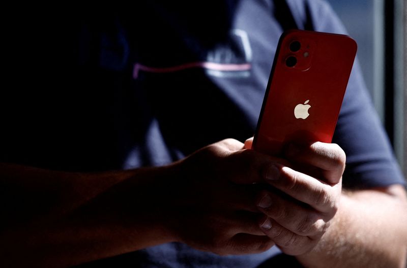 FILE PHOTO: A man poses with an Apple iPhone 12 in a mobile phone store in Nantes, France, September 13, 2023. REUTERS/Stephane Mahe/File photo