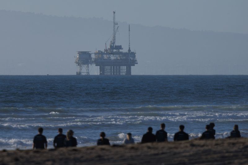 FILE PHOTO: An offshore oil rig is seen as a group of people help clean the beach in Huntington Beach, California, U.S., November 14, 2024.  REUTERS/Mike Blake/File Photo