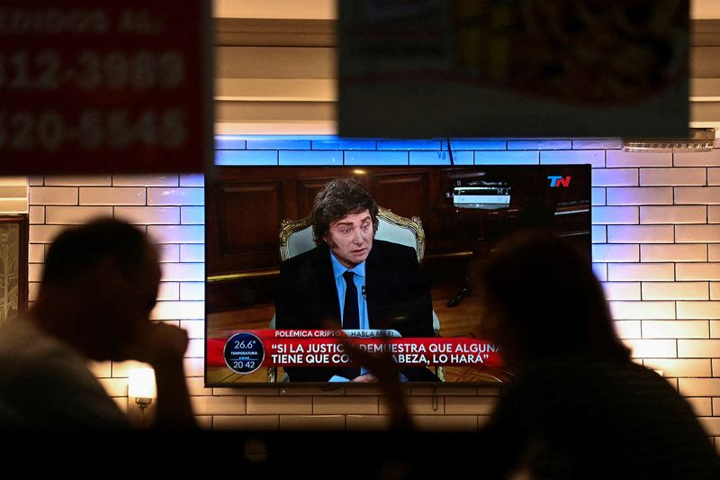 FILE PHOTO: People sit in a restaurant as Argentina’s President Javier Milei is seen on television, in Buenos Aires