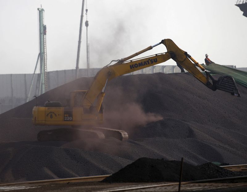 FILE PHOTO: A bulldozer and a labor work on a pile of iron ore at a steel factory in Tangshan in China’s Hebei Province