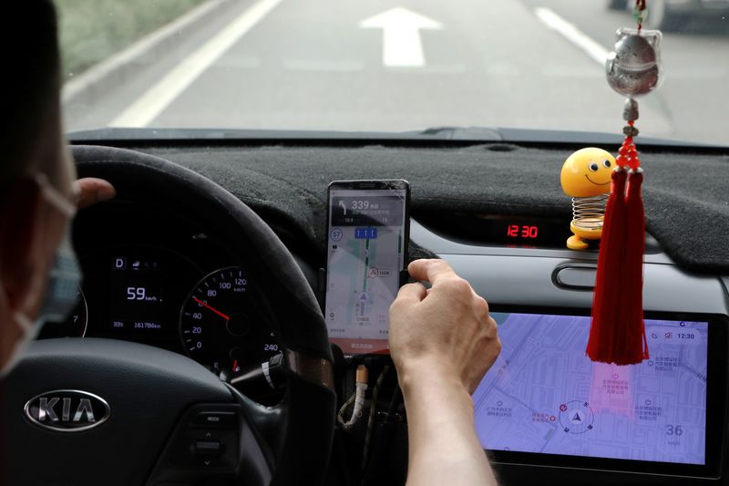 Driver of Chinese ride-hailing service Didi drives with a phone showing a navigation map on Didi’s app, in Beijing