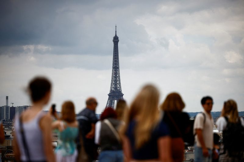 Tourists look at the Eiffel Tower and the Paris skyline from the rooftop of the Galeries Lafayette department store on a cloudy day in Paris