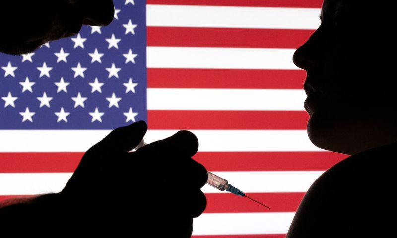 People pose with syringe with needle in front of displayed U.S. flag