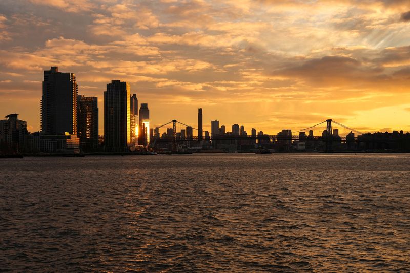 The sun sets behind the Lower Manhattan skyline in the Brooklyn borough of New York City