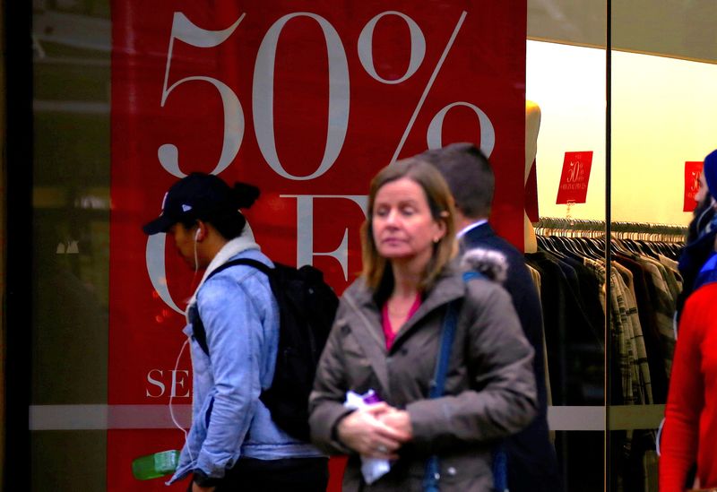 Shoppers walk past and stand outside a retail store displaying a sales sign in central Wellington, New Zealand
