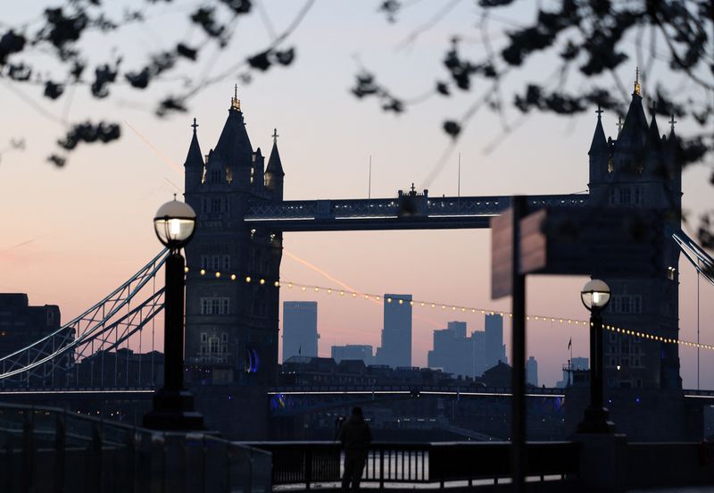 FILE PHOTO: A man takes photos as the sun rises behind Tower Bridge and the Canary Wharf financial district, in London, Britain, April 11, 2025. REUTERS/Isabel Infantes/ File Photo