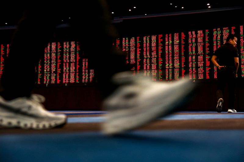 FILE PHOTO: People walk past an electronic board showing the stock index movements at a stock agent's office in Bangkok, Thailand, April 9, 2025. REUTERS/Athit Perawongmetha/ File Photo
