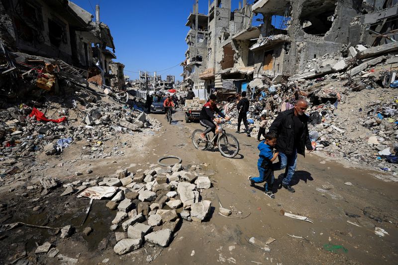 Palestinians pass by the rubble of destroyed houses, in Gaza City