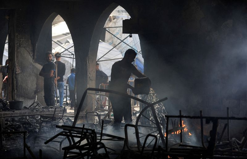 A Palestinian man throws water on a fire, as he inspects the damage at a school sheltering displaced people, following an Israeli strike, in Gaza City, April 23, 2025. REUTERS/Dawoud Abu Alkas