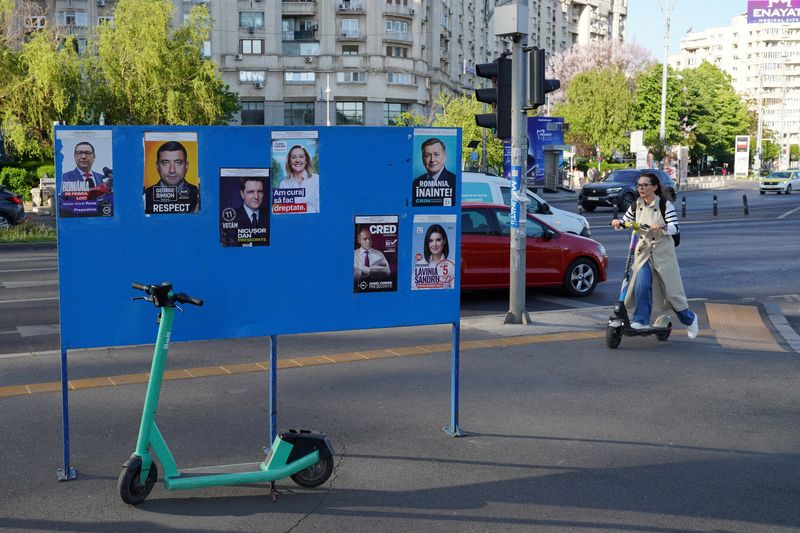 FILE PHOTO: A woman rides a scooter near electoral posters ahead of Romania's presidential elections, in Bucharest, Romania, April 29, 2025. REUTERS/Andreea Campeanu/File Photo