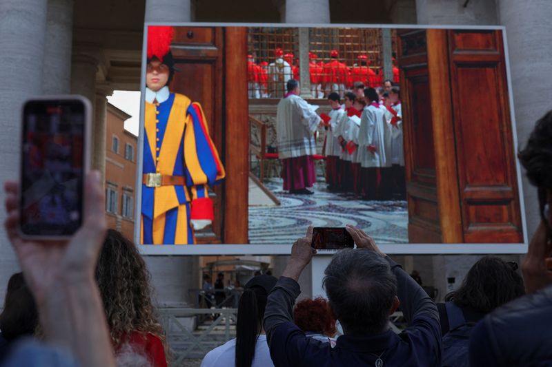 People gathered on St Peter's Square watch a screen showing Cardinals in the Sistine Chapel, on the first day of the conclave to elect the new pope, at the Vatican, May 7, 2025.  REUTERS/Amanda Perobelli