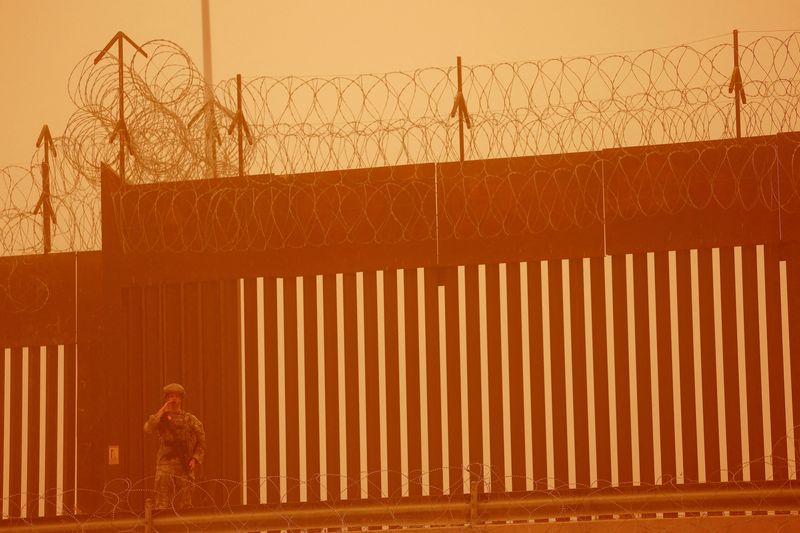 FILE PHOTO: A Texas National Guard soldier stands near the wall on the border between Mexico and U.S. during a sandstorm, as seen from Ciudad Juarez, Mexico March 6, 2025. REUTERS/Jose Luis Gonzalez/File Photo