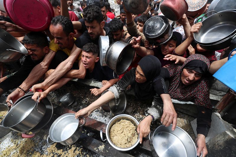 Palestinians wait to receive food cooked by a charity kitchen, in Jabalia, in the northern Gaza Strip, May 14, 2025. REUTERS/Mahmoud Issa