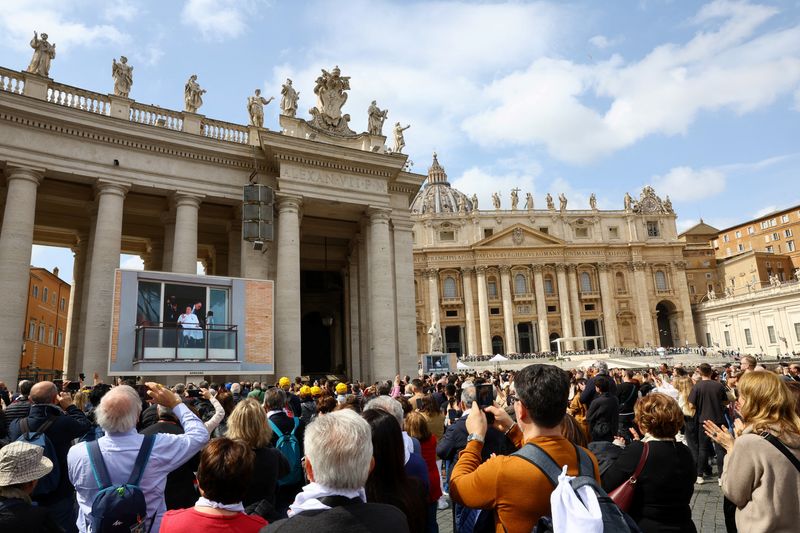 People watch Pope Francis appear from a window of Gemelli Hospital during his first public appearance in five weeks, on a big screen in St. Peter's Square, at the Vatican, March 23, 2025. REUTERS/Ciro de Luca/File Photo