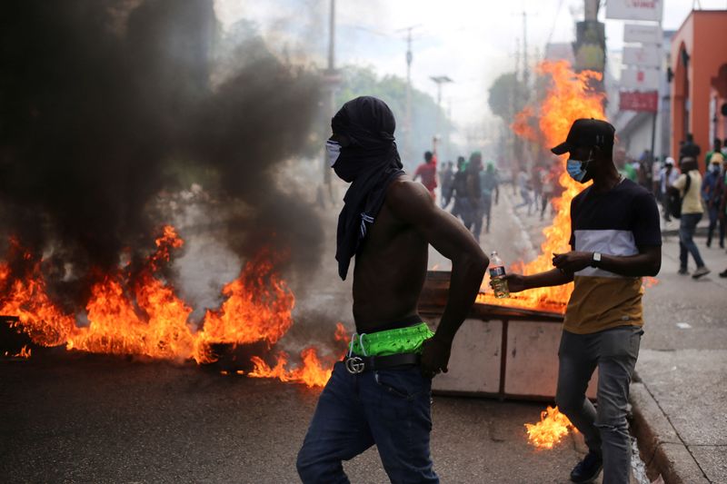 Demonstrators walk past a burning barricade during a protest against gang-related violence and to demand the resignation of Haiti's transitional presidential council, in Port-au-Prince, Haiti, March 26, 2025. REUTERS/Jean Feguens Regala