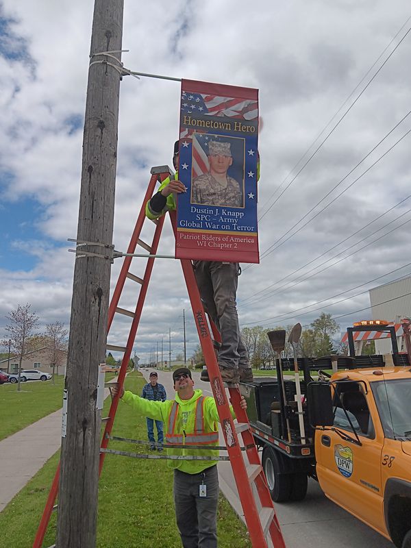 Crews hang a Salute to Service banner, a program organized by Shady Lane in Manitowoc, in May 2025.